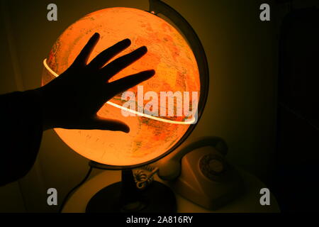 Earth globe lit up in the dark, with the silhouette of a hand in front of it Stock Photo