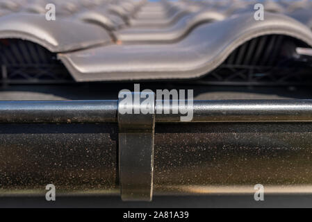 A metal, black gutter on a roof covered with ceramic tiles. Close up shot. Stock Photo