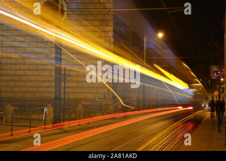 Night cityscape with vehicle like tram / bus in motion, colorful trails of lights. Stock Photo