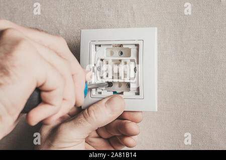A man mounts an electric light switch on the wall Stock Photo
