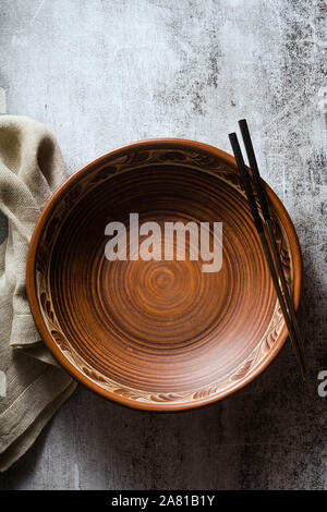 empty clay plate and chopsticks on a dark stone background. linen napkin Stock Photo