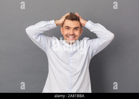 Freestyle. Young man studio standing isolated on grey holding head laughing cheerful Stock Photo