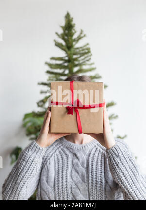 Woman hold a wrapped gift box with christmas tree. Craft paper wrapped box in hand with christmas tree at background. Concept of present surprise. Stock Photo