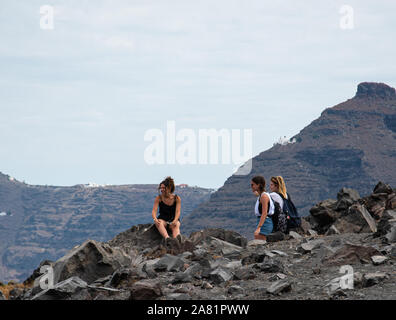 Nea Kameni Island, Greece - July 16 2019:   Three holidaymakers admire the view from a rest stop part way up the Volcanic mountain of Nea Kameni Stock Photo