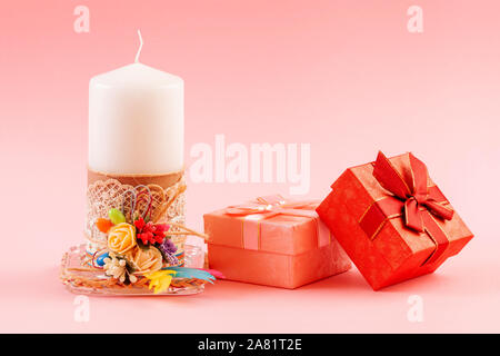 White decorated candle with two gift boxes on a pink background. Stock Photo