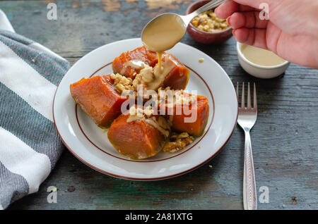 Pumpkin dessert , walnuts and tahini on wooden table.The woman is pouring tahini on the dessert. Stock Photo