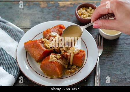 Pumpkin dessert , walnuts and tahini on wooden table.The woman is pouring tahini on the dessert. Stock Photo