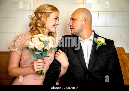 Close up of bride and groom in vintage clothing sitting and touching looking at each other with bride holding bouquet waiting to get married Stock Photo