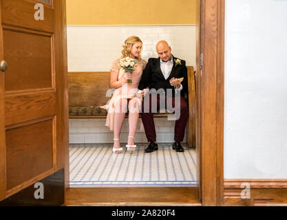 Image of couple  sitting awith man looking at marriage certificate at vintage style courthouse shot through doorway Stock Photo