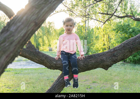 Sweet little kid girl sitting on the branch Stock Photo