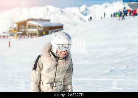 Portrait of young adult beautiful happy caucasian woman smiling near lift station at alpine winter skiing resort. Girl in fashion ski suit, goggles Stock Photo