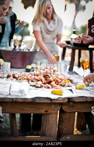 People standing around a table of fresh seafood at an outdoor dinner party Stock Photo