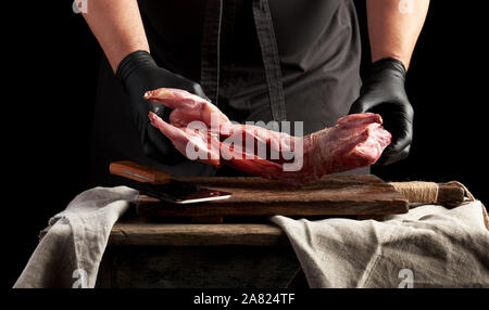 chef in black latex gloves holds a whole rabbit carcass on a brown cutting board, process of cooking meat Stock Photo