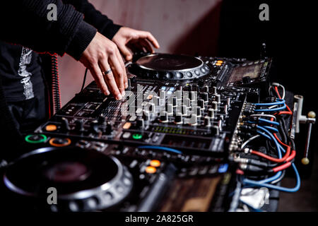 DJ plays live set and mixing music on turntable console at stage in the night club. Disc Jokey Hands on a sound mixer station at club party. DJ mixer Stock Photo