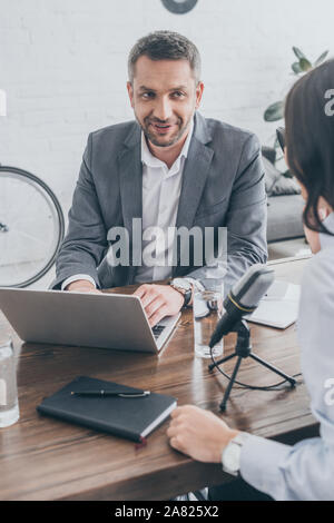 smiling radio host using laptop while interviewing businesswoman in broadcasting studio Stock Photo