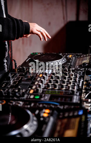 DJ plays live set and mixing music on turntable console at stage in the night club. Disc Jokey Hands on a sound mixer station at club party. DJ mixer Stock Photo