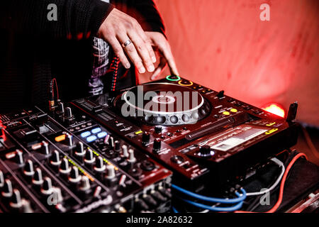 DJ plays live set and mixing music on turntable console at stage in the night club. Disc Jokey Hands on a sound mixer station at club party. DJ mixer Stock Photo