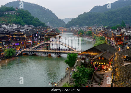 Traditional Chinese architecture flanks the tower footbridge over the Tuo Jiang River in Fenghuang Ancient City in Tibet. Stock Photo
