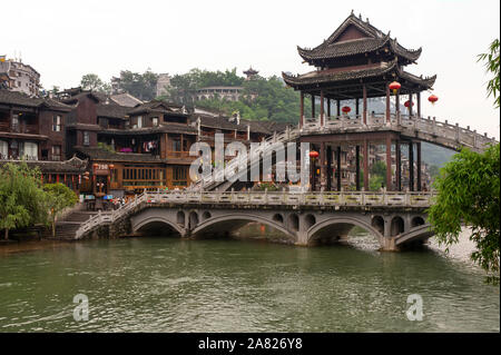 Tourists cross the Nanhua Bridge over the Tuo Jiang River to admire the historic significance of Fenghuang Ancient City in the autonomous region of Ti Stock Photo