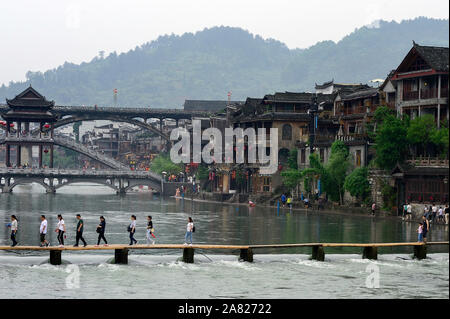 Tourists utilize a footpath that crosses the Tuo Jiang River independent of the Nanhua Bridge to its side in UNESCO World Heritage site Fenghuang Anci Stock Photo