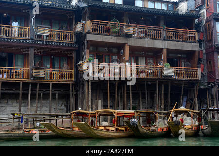 A man in Fenghuang Ancient City peers over his apartment balcony at a row of tour boats in the Tuo Jiang River below. Stock Photo