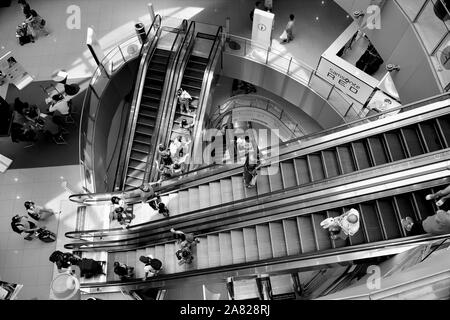 Singapore - September 29 2019: Aerial view of modern escalator shaft at Vivo City shopping centre with shoppers in monochrome. Stock Photo