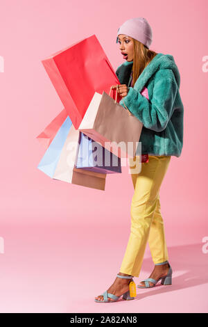 surprised, trendy african american woman looking in shopping bag on pink background, fashion doll concept Stock Photo