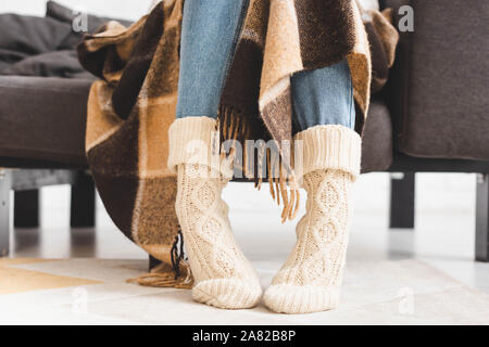 cropped view of girl in knitted socks sitting in blanket on sofa Stock Photo