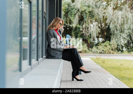side view of attractive businesswoman in coat using laptop Stock Photo