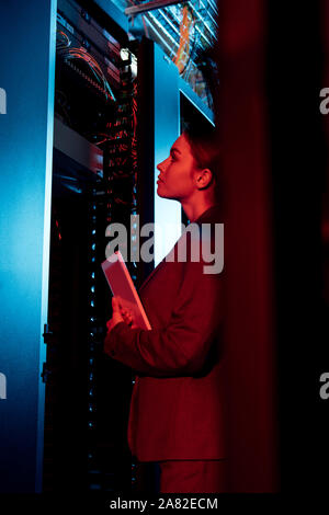 selective focus of attractive businesswoman looking at server rack and holding digital tablet Stock Photo