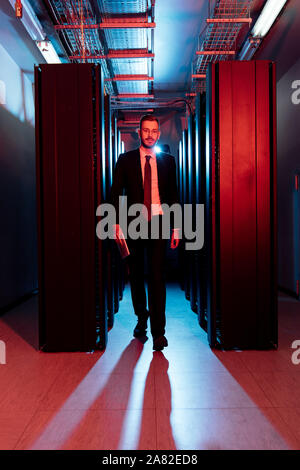 bearded businessman in glasses holding digital tablet and walking in server room Stock Photo