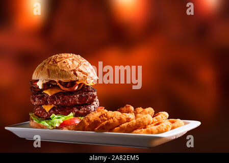 Hamburger double burger cheese bacon tomato lettuce onion rings, isolated on an out of focus wooden fire background Stock Photo
