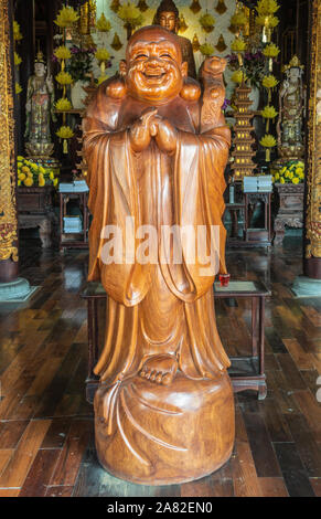 Da Nang, Vietnam - March 10, 2019: Chua An Long Chinese Buddhist Temple. Brown Wooden laughing Buddha statue at entrance to sanctuary. Stock Photo