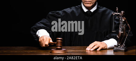 panoramic shot of judge in judicial robe sitting at table and hit with gavel isolated on black Stock Photo