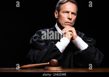 judge in judicial robe sitting at table with gavel isolated on black Stock Photo