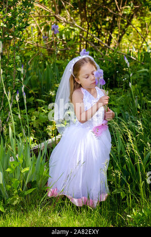 child in a little bride outfit is smelling iris flowers in a garden Stock Photo