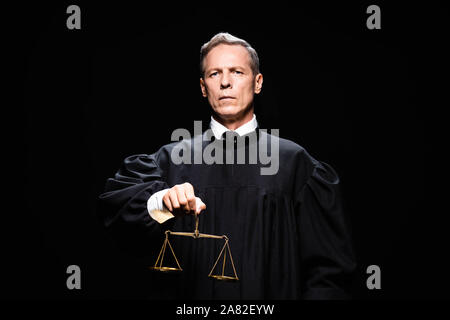 judge in judicial robe holding scales of justice isolated on black Stock Photo