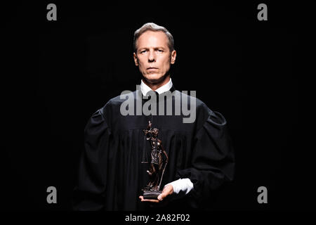 judge in judicial robe holding themis figure isolated on black Stock Photo
