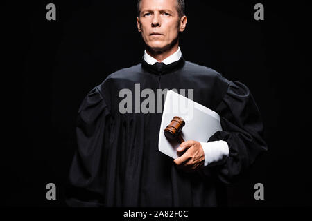 judge in judicial robe holding gavel and papers isolated on black Stock Photo