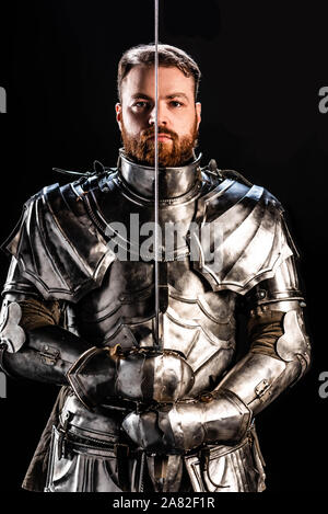 handsome knight in armor holding sword isolated on black Stock Photo