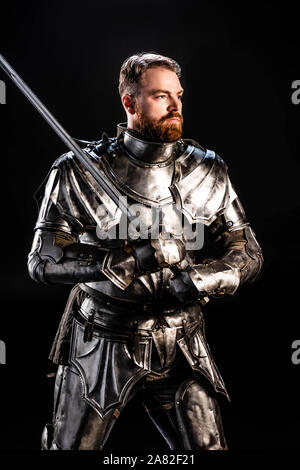 handsome knight in armor holding sword isolated on black Stock Photo