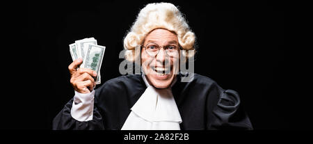 panoramic shot of smiling judge in judicial robe and wig holding money isolated on black Stock Photo