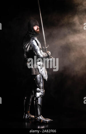 handsome knight in armor holding sword on black background Stock Photo