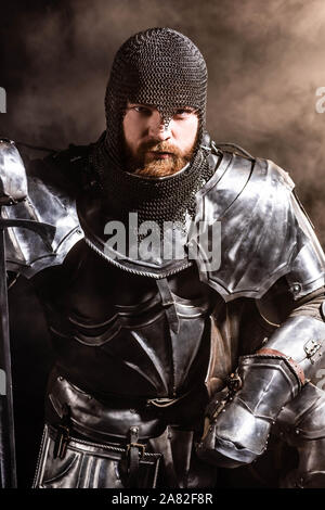 handsome knight in armor holding sword on black background Stock Photo