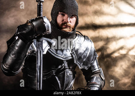 handsome knight in armor holding sword on black background Stock Photo