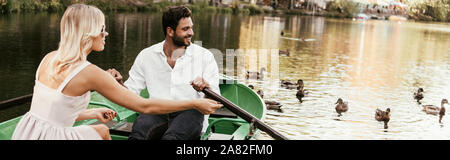 panoramic shot of young couple in boat on lake near flock of ducks Stock Photo