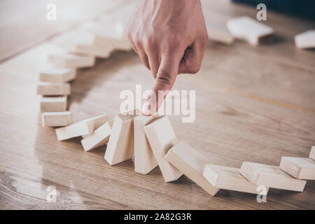 cropped view of businessman stopping domino effect of falling wooden blocks Stock Photo