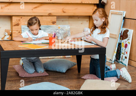 cute kids drawing on papers while sitting on pillows Stock Photo
