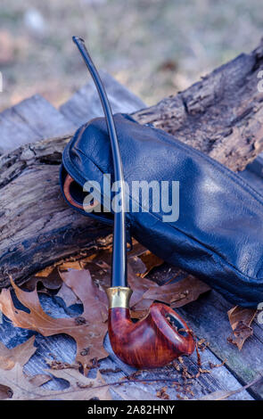Churchwarden pipe with leather tobacco pouch on a rustic outdoor background Stock Photo