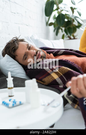 Sick man lying in bed with medicines on table at home Stock Photo